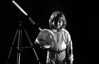 Astronot başlığı ve teleskop takan küçük bir çocuk. Astronotun içinde oynayan ve uzay adamı olmayı hayal eden sevimli bir çocuk. Astronomi ve astroloji kavramı