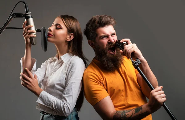 Singing man and young woman in a recording studio. Expressive couple with microphone. Happy friends with excited faces enjoy music