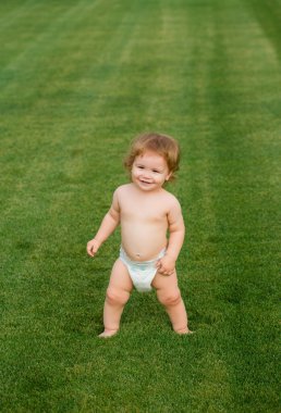 Yaz akşamında çimlerin üzerinde mutlu bir bebek. Dışarıda gülümseyen bir çocuk. Mutlu çocukluk ve çocuk sağlığı hizmetleri