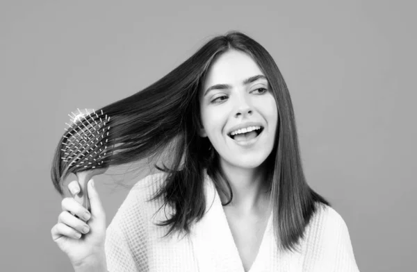 Amazed woman combing hair. Portrait of female model with a comb brushing hair. Girl with hairbrush, hair care and beauty