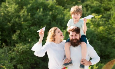 Mutlu bir aile. Anne ve baba, yaz aylarında doğada oyuncak kağıt uçakla çayırda. Baba, anne ve oğul birlikte oynuyorlar. Çocuk Bakımı