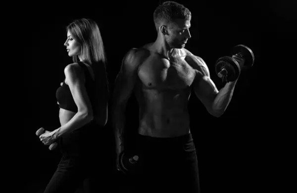 Muscular couple body in studio. Couple of fit bodybuilders, muscular man and beautiful sexy girl with dumbbells. Sport couple