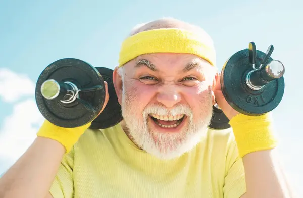 Senior man in his seventies training and lifting weigh. Health club or rehabilitation center for elderly aged pensioner. Senior sport man lifting dumbbells in sport center
