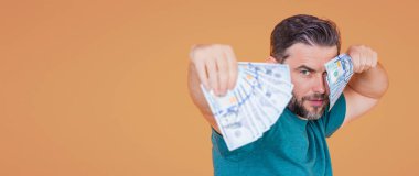 Bej renkli stüdyo pankartına para yatıran adam. Dolar banknotları olan takım elbiseli zengin bir adam. Dolar banknotlarıyla başarılı bir iş adamı