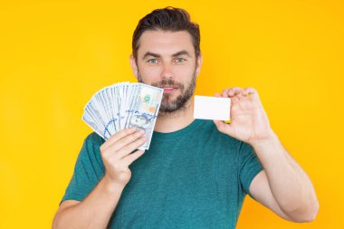 İyi ödeme. Yakışıklı adam gri stüdyoda izole edilmiş para tutuyor. Dolar banknotları halinde para. Yığınla para, finans, yatırım ve tasarruf