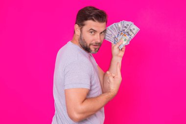 Yakışıklı orta yaşlı adam pembe stüdyoda izole edilmiş para tutuyor. Dolar banknotları halinde para. Yığınla para, finans, yatırım ve tasarruf. Model pankart, ödeme konsepti