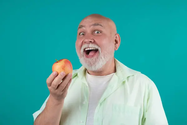 Funny Senior granddad eat apple in studio. Portrait of a elderly man eating an apple. Man biting apple. Apple fruit for aged people. Senior on diet and healthy lifestyle. Portrait senior with apples