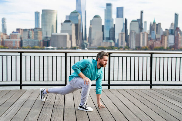 Mature sportsman outdoor workout, man enjoying active lifestyle outside in NYC. Man doing stretching exercise, preparing for workout near Manhattan. Sporty athletic fit man 40s wear sports clothes