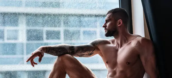 Handsome muscular man in bedroom on window curtains. Young handsome sexy man resting at home. Guy with athletic muscles. Sexy young handsome naked man on bedroom. Seductive gay