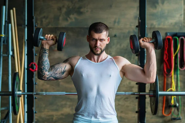 Fit guy doing exercise at gym. Handsome sporty man workout with with dumbbells on gym. Male athlete with dumbbell on fitness workout. Fitness man in gym. Muscular sportsman workout with weight in gym