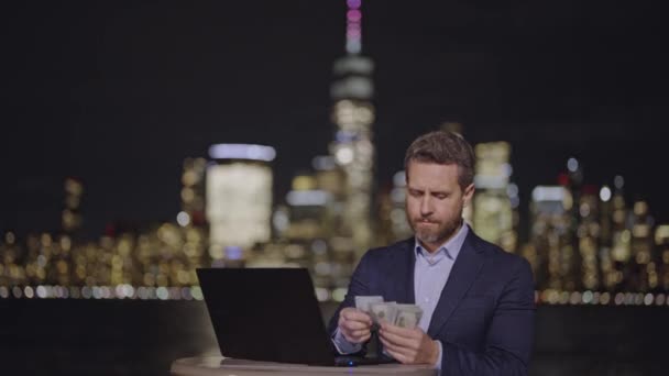 穿着西装的人在纽约市用笔记本电脑数着我们的美元钞票 商人在夜市数着美国钞票 成功的商人在曼哈顿夜晚的背景下计算现金 — 图库视频影像
