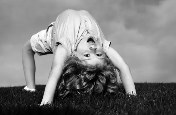幸せな少年は夏の日差しの中で草の上に立っている 公園の芝生の上で逆さまに立って面白い幸せな小さな子供 幼少期のコンセプト キッズスポーツ — ストック写真