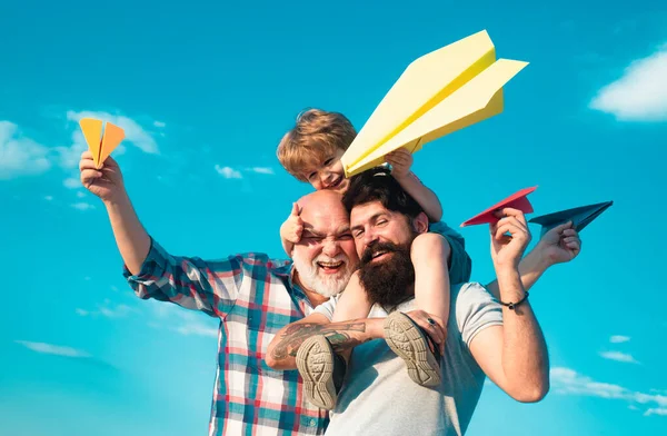 Happy three generations of men have fun and smiling on blue sky background. Enjoy family together. Dream of flying. Kids playing with simple paper planes on sunny day