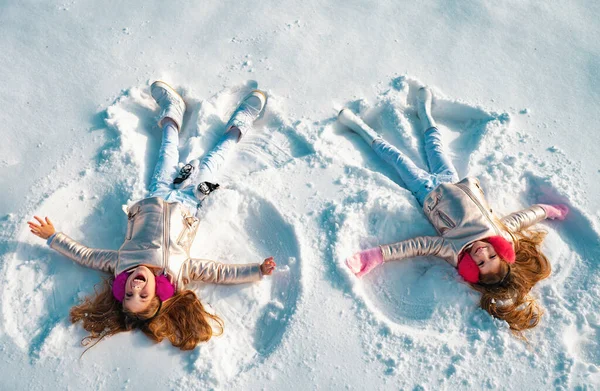 雪の天使の幸せな女の子が示しています 雪の上に横たわっている間に雪の天使を作る2人の女の子 — ストック写真