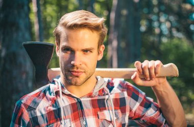 Sakallı yakışıklı bir genç adam ağaç taşır. Yakışıklı Woodworkers oduncu ekose gömlek yeşil doğa arka plan üzerinde balta tutan