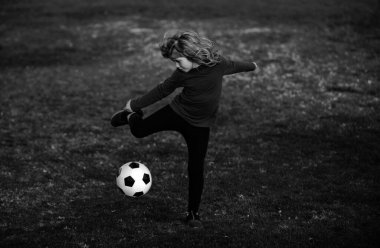 Futbolcu. Çocuklar yaz stadyum sahasında futbol oynarlar. Küçük çocuk topa vuruyor. Çocuk futbol topunu tekmeliyor. Futbol topuyla uçan tekme atan genç çocuk.