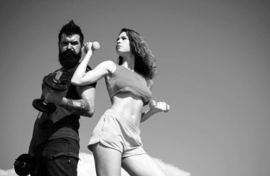 Fit çift dışarıda halterle egzersiz yapıyor. Sağlıklı yaşam tarzı konsepti, spor. Dambıllarla egzersiz yapan seksi çift. Güçlü erkek ve seksi kadın arka planda dambıllarla çalışıyor.