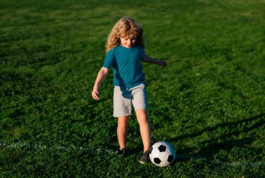 Futbolcu çocuk futbol oynuyor. Çocuk çimlerin üzerinde futbol topunu tekmeliyor. Futbol antrenmanı sırasında sporcu çocuk.