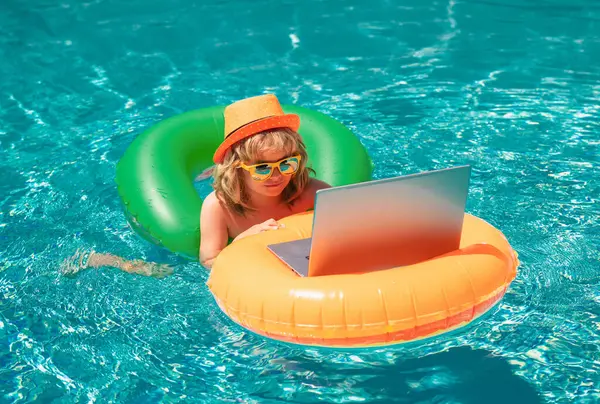 Yaz işleri ve online teknoloji. Küçük mutlu çocuk çevrimiçi bilgisayar bilgisayarı öğreniyor. Çocuk yüzme havuzundaki bilgisayarı kullanarak yüzer halkada rahatlar.