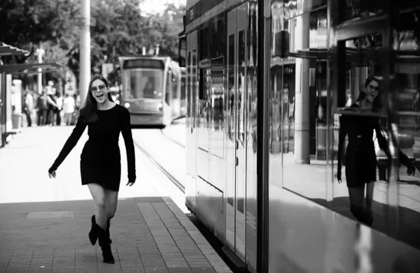 Fashionable woman running after bus trolleybus and pulling trolley case on the street, fashion street style