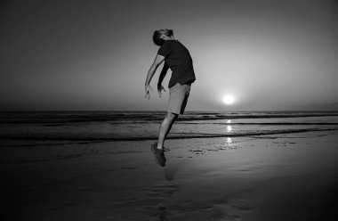 Sahilde atlayan bir adam, gün batımında siluet. İyi ve özgürlük kavramı
