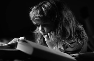 Yatakta uzanmış kitap okuyan sevimli bir çocuk. Çocuğun gelişimi. Akıllı çocuk.