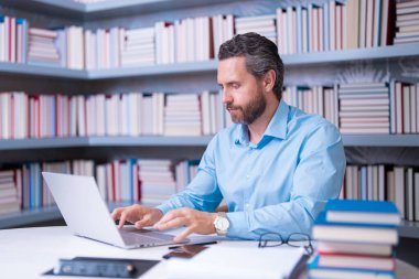 Kütüphanede kitabı olan bir öğretmenin portresi. Üniversitede yakışıklı bir öğretmen. Öğretmenler Günü. İyi bir öğretmen. Üniversitede öğretmen. Kütüphanede kitapları olan bir adam. Bilgi ve eğitim kavramı