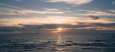 Denizde gün batımı. Sakin bulutlu gökyüzü ile okyanus sahili gündoğumu