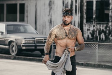 Suç sokağında dövmeli gangster. İspanyol suç çetesi üyeleri. Gangsta Crimes tarzı. İspanyol bir hırsız. Etnik kızgın suç adamı. Dışarıdaki güçlü vücutta dövmesi olan bir suçlu. Sokak tarzı