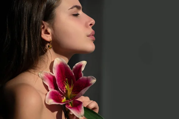 Youth and skin care concept. Beauty girl with lily. Beautiful sensual woman hold flowers, studio portrait
