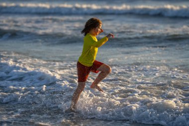 Heyecanlı çocuk yaz denizinde su sıçratarak oynuyor. Yaz tatili. Çocuk denizde dalgalarla oynuyor. Küçük çocuk denizde oynuyor ve su damlaları sıçrıyor. Çocuk denizde su sıçratmaca oynuyor. Yaz tatili