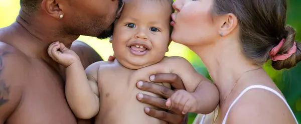 Mixed race family portrait. Happy multiracial family outside. International family mom and dad with little biracial child. Family of African american father carrying little baby. Happy parents