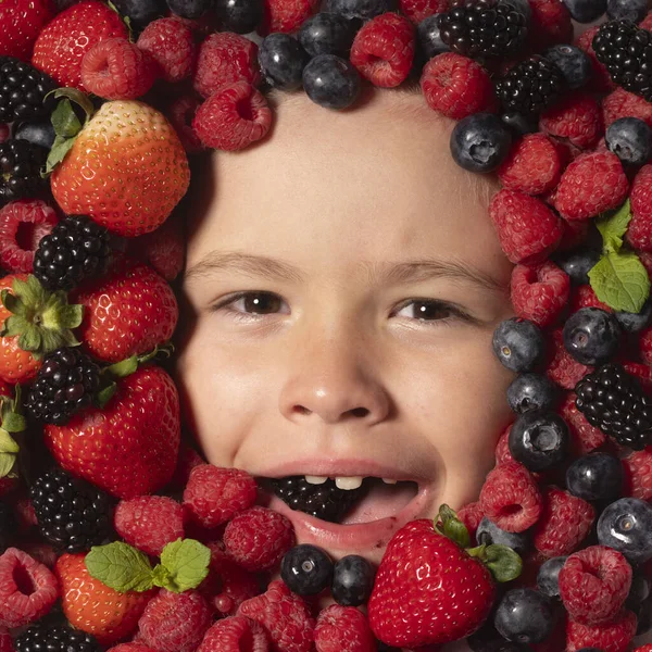 Healthy food for kids. The kids face with fruit and berries. Summer strawberry, blueberry, raspberry, blackberry background. Top view photo of child face in berries background. Healthy kids eating