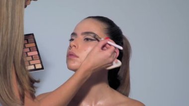Profesyonel makyöz güzel genç bir kadınla çalışıyor. Seksi mankeni telafi et. Makyaj sanatçısı güzel makyaj yapıyor. Profesyonel makyöz, cazibe modeli makyajı yapıyor.
