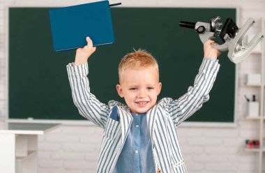 School child student learning in class. Education and kids knowledge concept. Portrait of schoolboy in classroom near blackboard. Excited schoolboy pupil with microscope and book