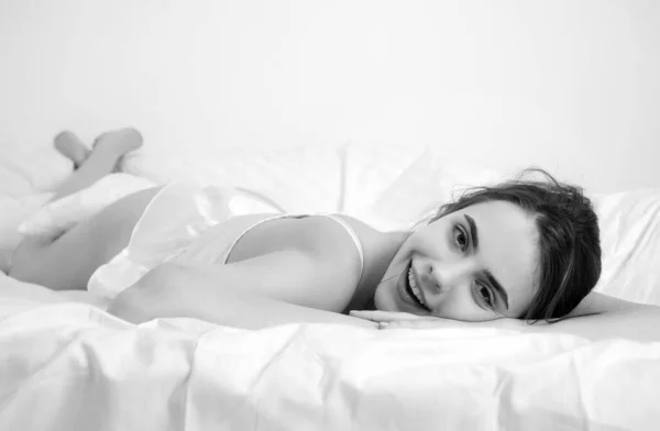 Young woman in bed. Portrait of beautiful female resting on bed with pillows in white bedding in bedroom in morning. People sleep