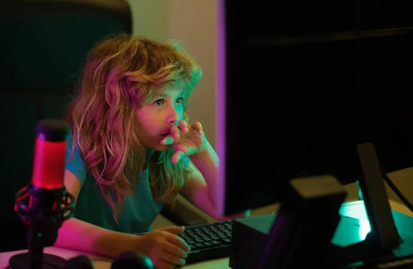 Child playing computer games or studying on pc computer. Kid gamer on night neon lighting. Child using computer technology in home