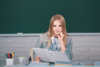 Female college student reading book in classroom, preparing for exam