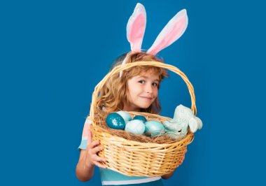 Mutlu Paskalyalar. Paskalya sepeti olan çocuk mavi arka planda izole edilmiş. Komik çocuk suratı