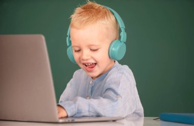Kulaklıklı mutlu çocuk dizüstü bilgisayar kullanıyor ve okuldaki video öğretmeniyle internetten ders çalışıyor. Uzaktan eğitim ve eğitim