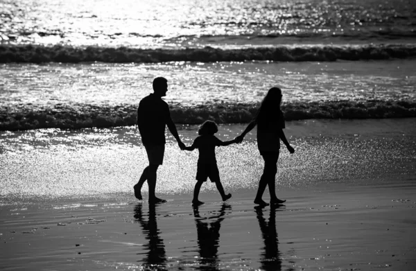 Silhouette of father, mother and child son holding hands and walking on beach. Sctive fanily lifestyle, parents with children on summer vacations