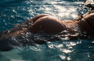 Sexy buttocks in pool closeup, summer journey, sensual woman with hot natural butt relax in water. Wet body, ass in sexy bikini. Seduction and pleasure model. Luxury passion buttocks