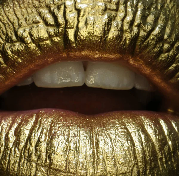 Macro close up gold lips. Gold paint from the mouth. Golden lips on woman mouth with make-up. Sensual and creative design for golden metallic
