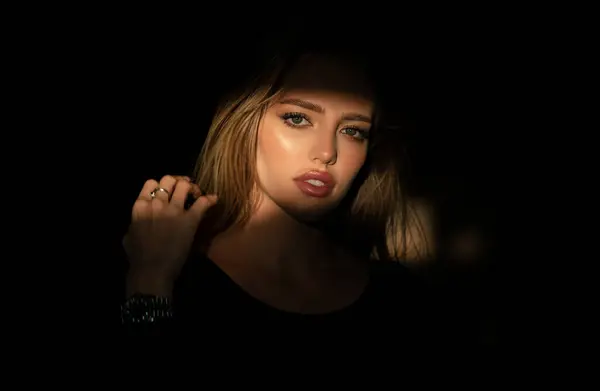 Elegant young woman posing over black background. Light and shadow. Portrait of a beauty woman face. Creative portraits with shadow and light over womans face, eyes on light