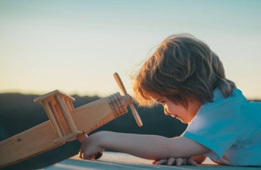 Mavi gökyüzü arka planında oyuncak uçakla oynayan mutlu çocuk. Güneşli bir yaz gününde yürüyen sevimli bir çocuk. Çocuklar seyahat hayali kurar.