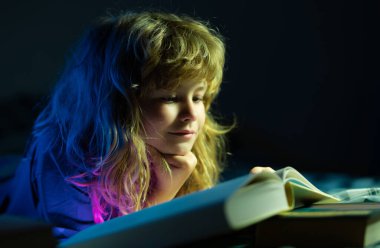 Çocuk masal okuyor, karanlık oda fotoğrafı. Çocuk kitap okuyor. Çocuklar yatma vakti, çocuk yatakta kitap okuyor.