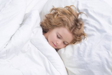 Çocuk rahat beyaz bir yatakta uyuyor. Sarışın, beyaz bir çocuğun güzel yüzü, yatakta uyuyor. Tatlı rüyalar. Küçük bebek evde yatarken uyuyor.