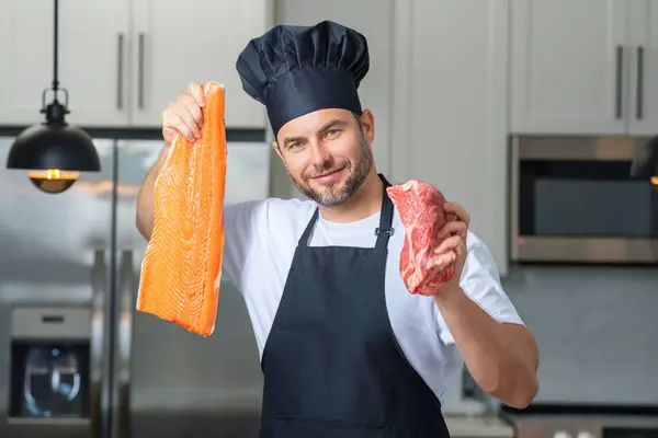 Health, natural protein. Handsome man in kitchen cooking fish and meat, salmon and beef in the kitchen. Healthy food concept. Healthy diet, meat protein. Raw fish and meat