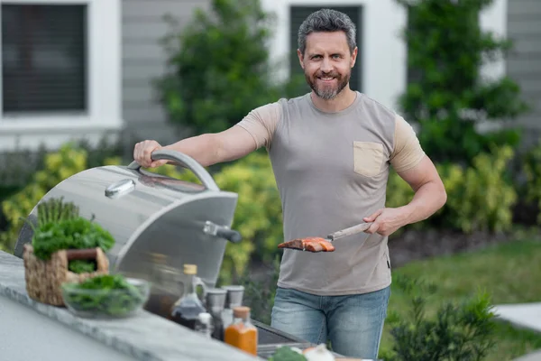 stock image Male chef grilling and barbequing in garden. Barbecue outdoor garden party. Handsome man preparing barbecue meat. Concept of eating and cooking outdoor during summer time