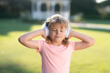 Çocuk kulaklıkla müzik dinliyor. Yaz parkındaki sevimli çocuk müzikten hoşlanıyor, hayal kuruyor ve dinleniyor. Çocuklar boş zamanlarını favori müziklerle geçirirler.